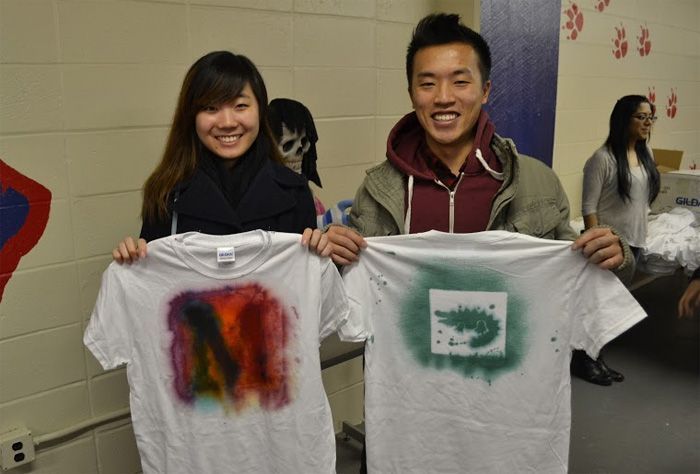 Students, Benjamin Qiu, a senior engineering major, and Ming Cheung, a senior occupational therapy major, hold up their own t-shirts.