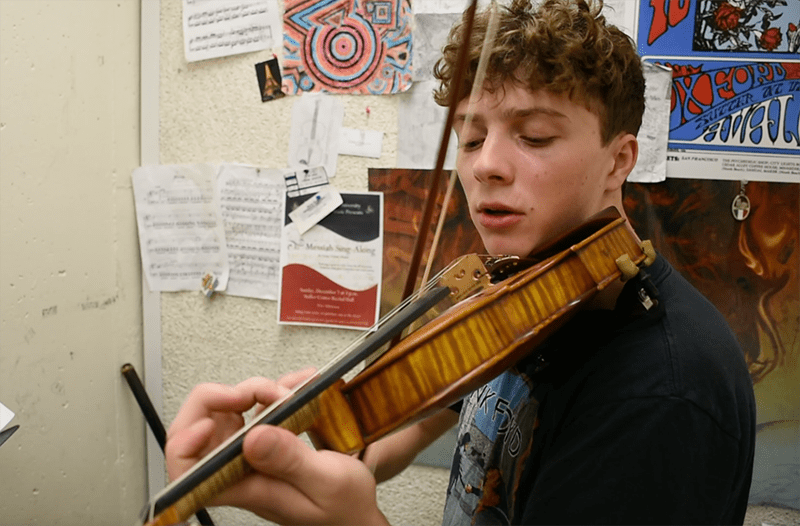 Stony Brook student Samuel Vodopia is playing violin in a practice room.